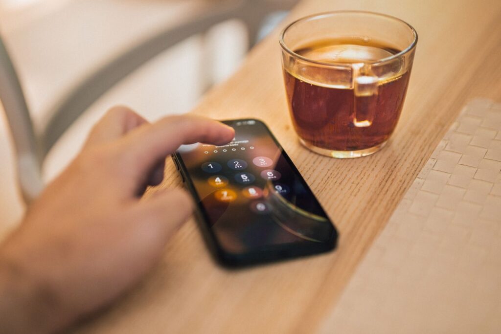 Hånd låser en smartphone op ved siden af en kop te
